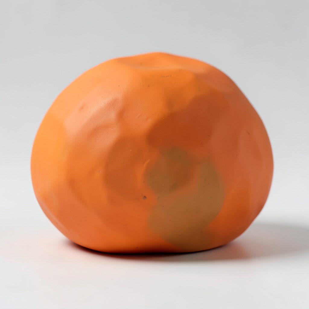 Soft clay-model portrait of a rounded head and shoulders figure in muted teal and warm orange.