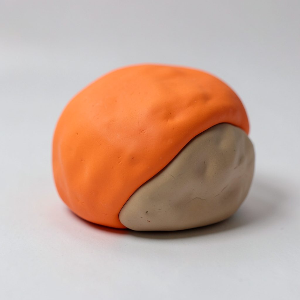 Soft clay-model portrait of a rounded figure with warm sand and orange tones.
